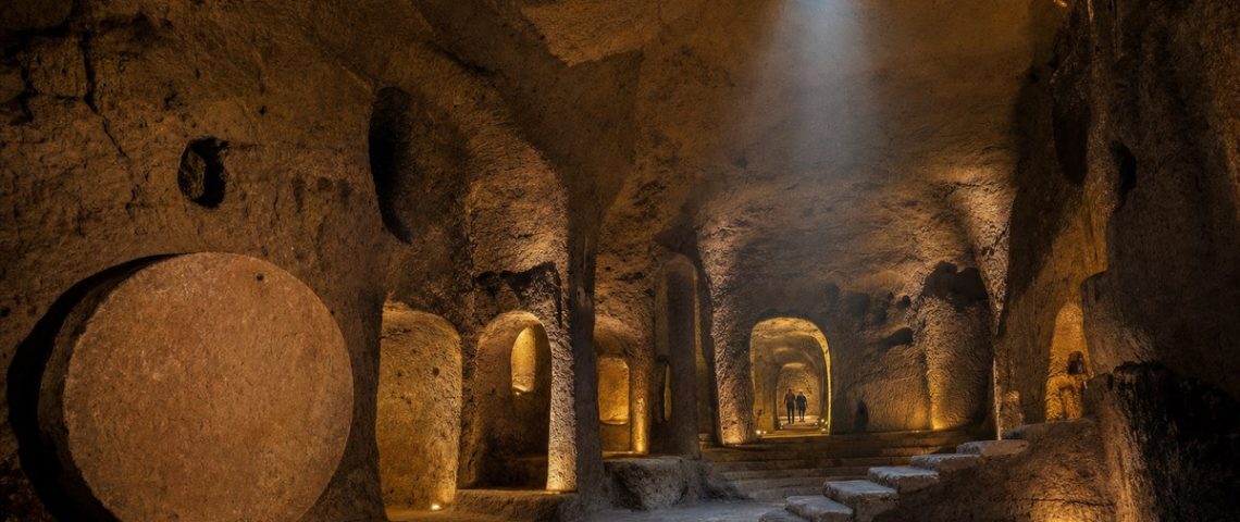 Sală vastă săpată în rocă vulcanică într-un oraș subteran, cu ușă circulară de piatră și pasaje luminate
